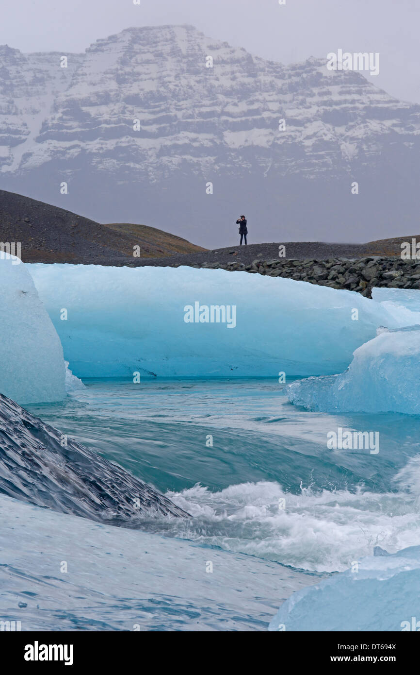 Vista attraverso il deflusso della laguna glaciale Islanda con una sola persona stagliano sulla riva lontana Foto Stock