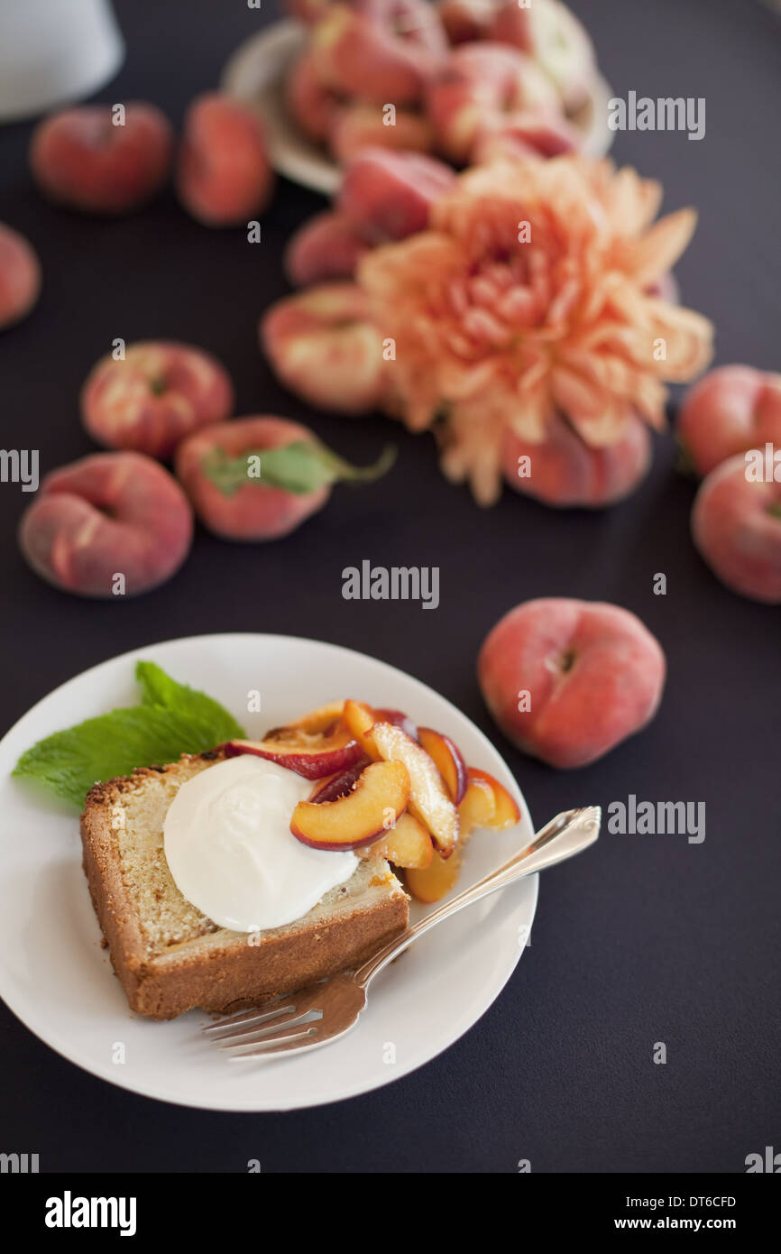 Frutta e fiori freschi. Una fetta di organico peach torta con un serving di crème fraiche e pesche ciambella. Foto Stock