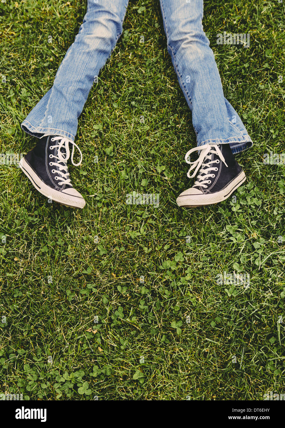 Una ragazza di 10 anni sdraiati sull'erba. Vista ritagliata della sua parte inferiore delle gambe. Indossare scarpe da ginnastica e sbiadita blue jeans. Foto Stock
