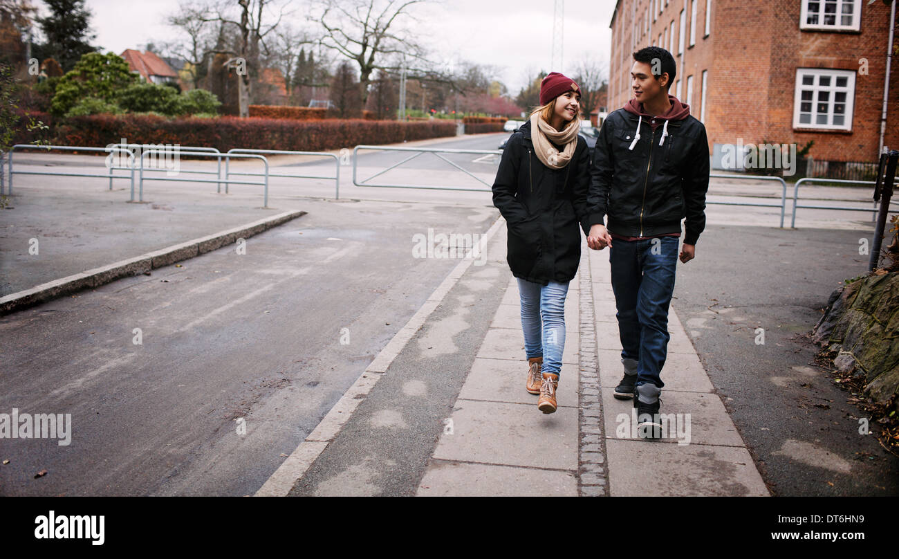Coppia giovane camminando su un marciapiede tenendo le mani guardando ogni altro su un giorno d'inverno. Asian teenage l uomo e la donna a piedi. Foto Stock