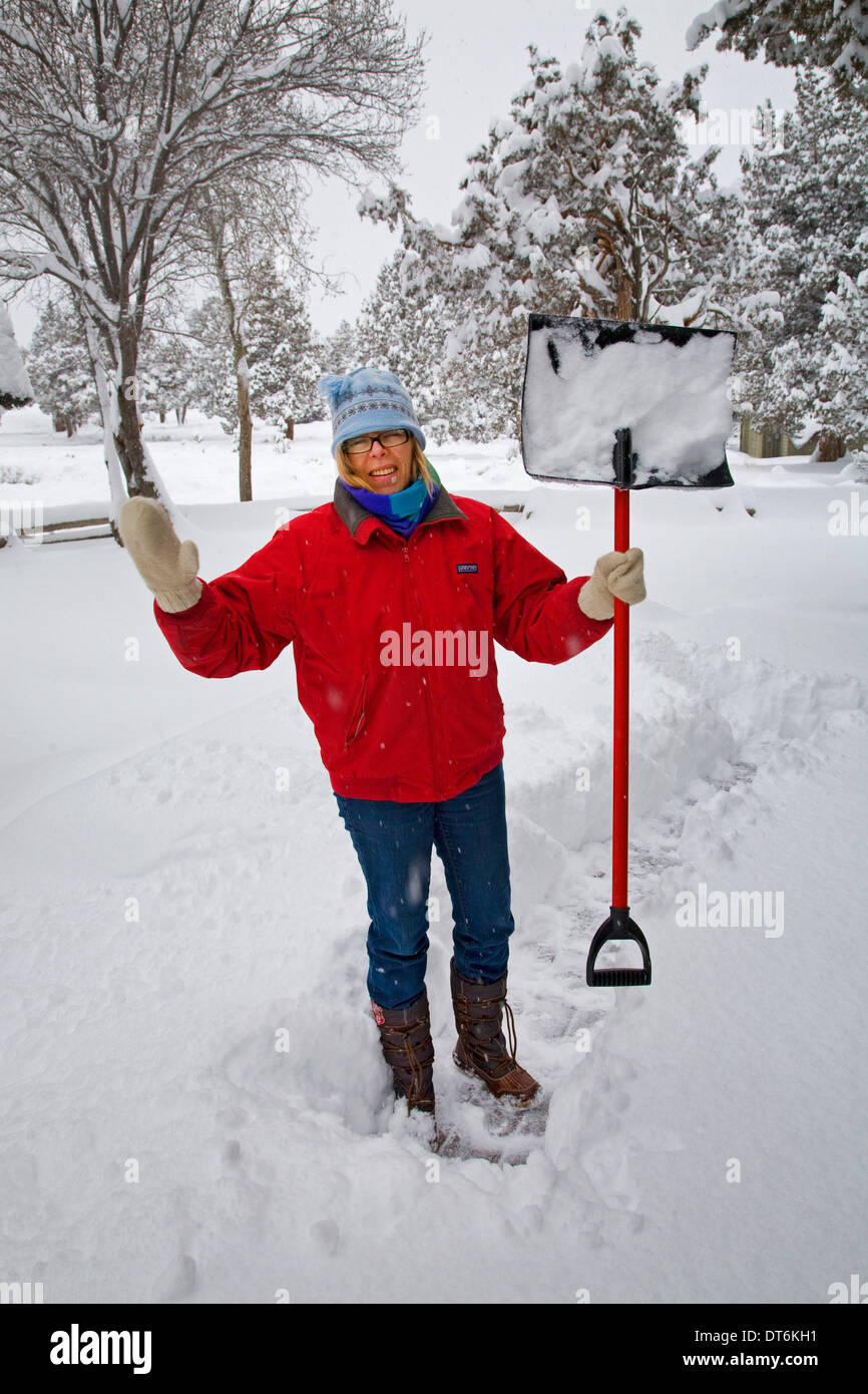 Una donna spalare la neve dal suo deck o portico anteriore in corrispondenza di una casa di campagna nel centro di Oregon durante una forte tempesta di neve. Foto Stock