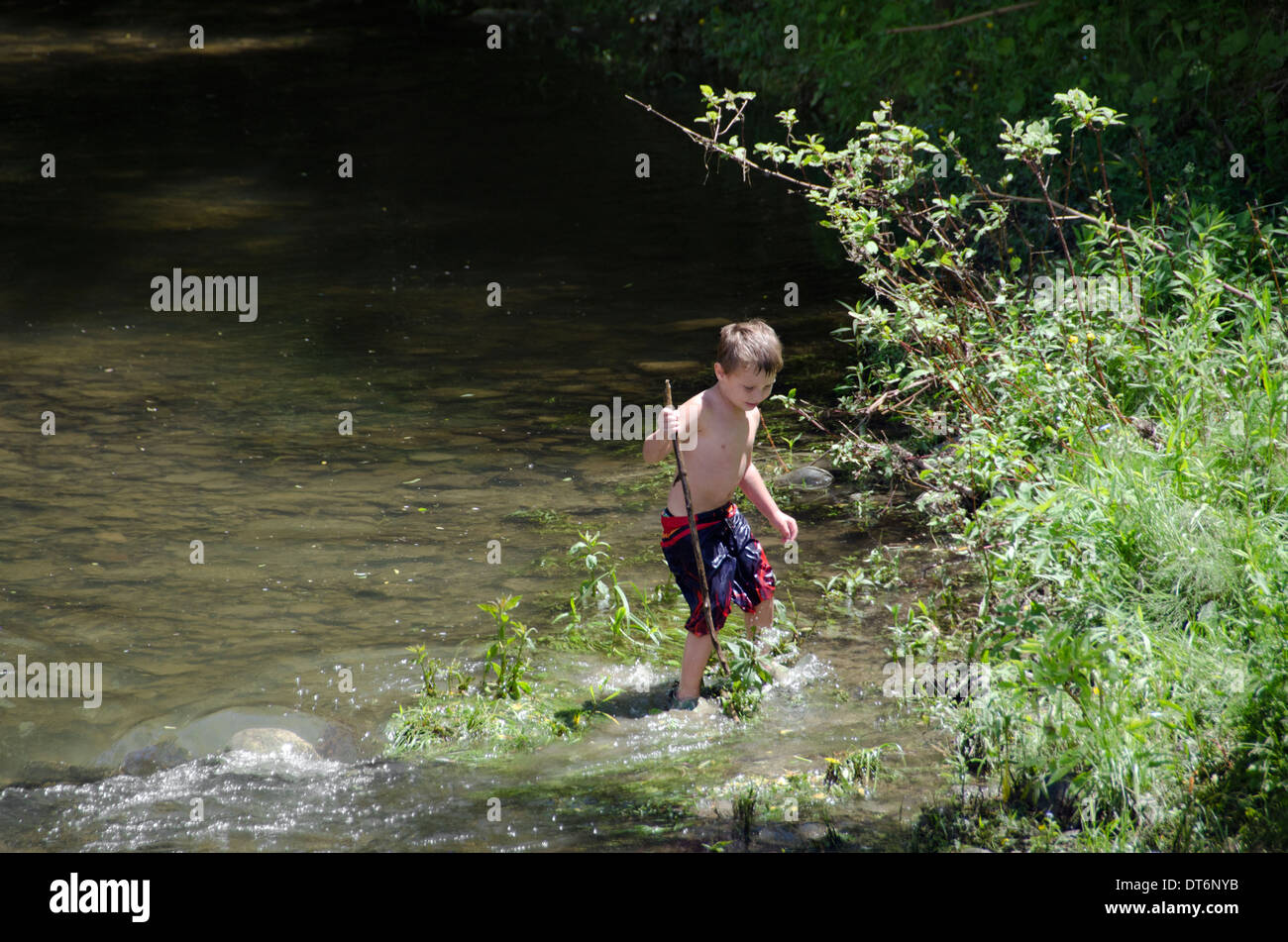Un giovane ragazzo giocando in un fiume creek Foto Stock