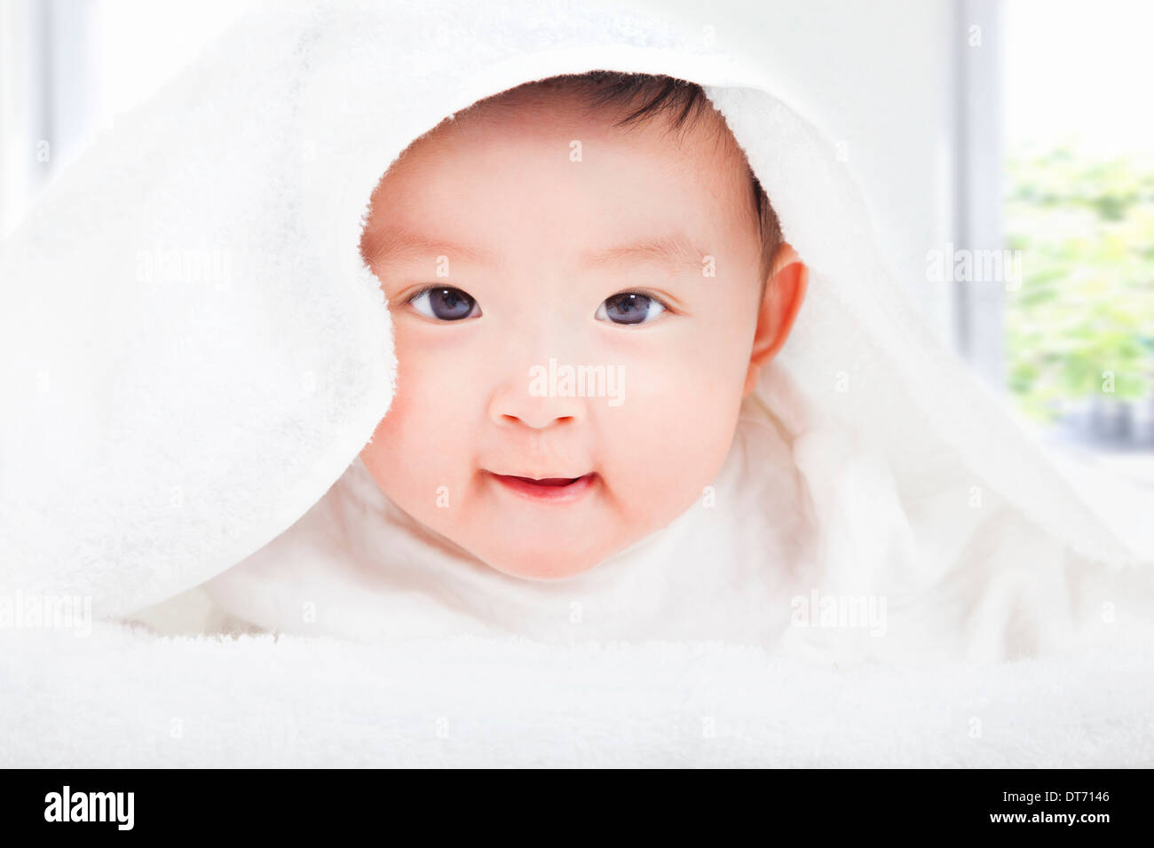 Bambino sorridente sorridente sotto una coltre bianca o asciugamano a casa Foto Stock