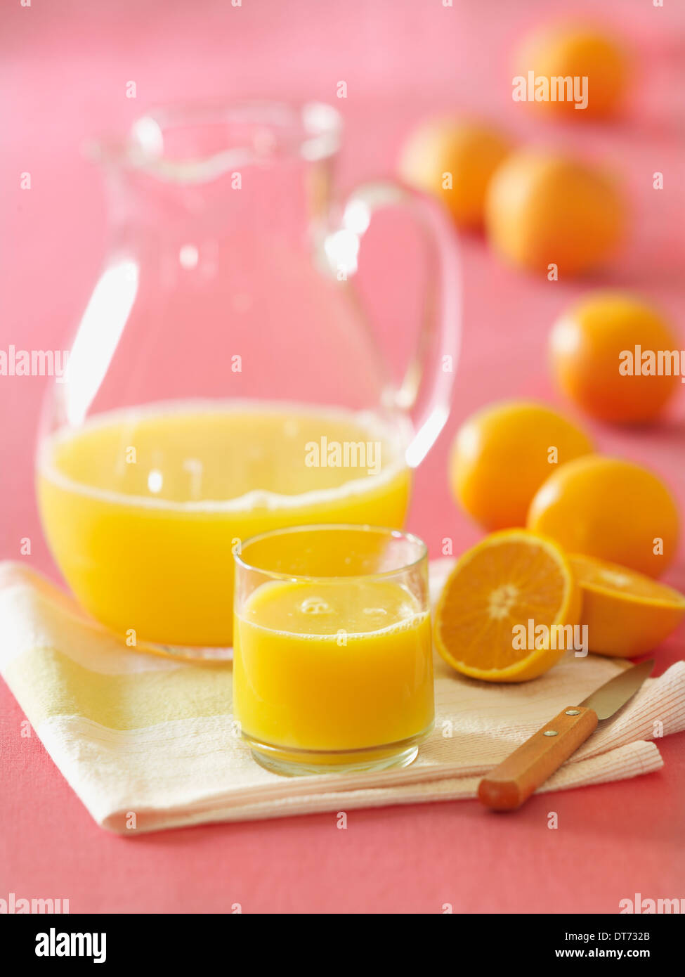 Una brocca di vetro di succo di arancia con un bicchiere riempito con succo di frutta appena spremuto con diversi arance in background. Foto Stock