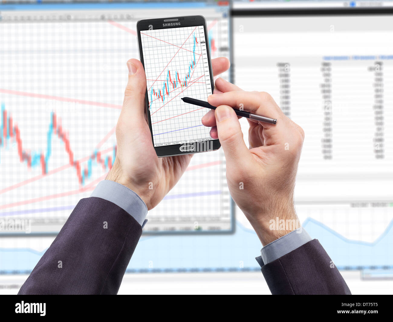 Imprenditore con smartphone visualizzazione cambio valuta grafici e un monitor in background Foto Stock