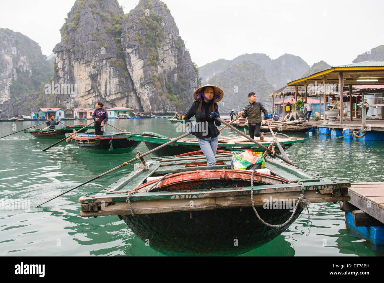 Una donna nel cappello conico e western dress righe una barca di bambù per i turisti in un galleggiante villaggio di pescatori. Foto Stock