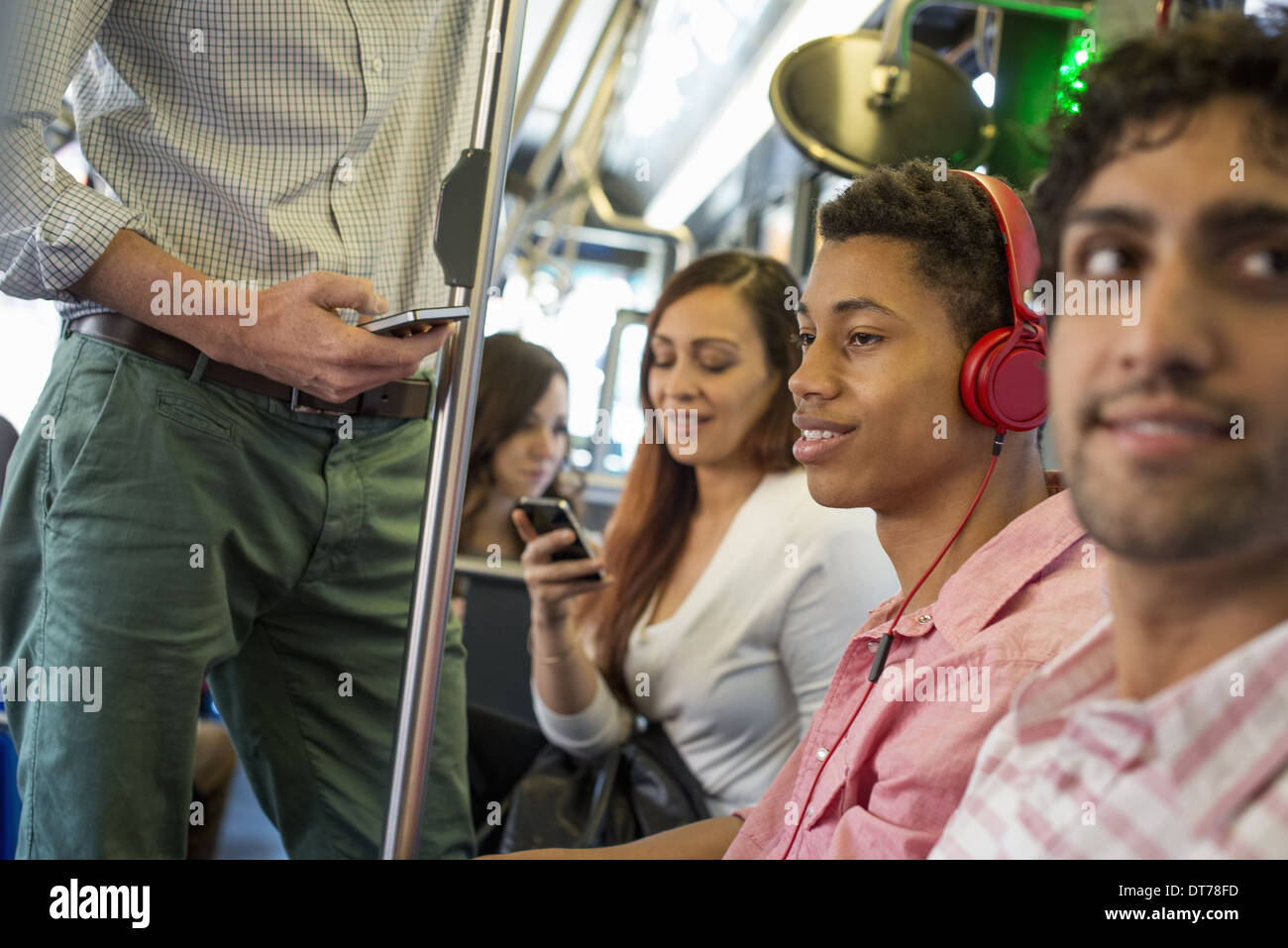 Gli uomini e le donne su un autobus cittadino, nella città di New York. Un uomo con le cuffie a. Un uomo e una donna di controllare i loro telefoni intelligenti. Foto Stock