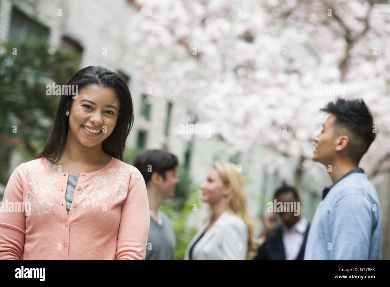 La vita della città in primavera. I giovani all'aperto in un parco della città. Una donna in maglia rosa con quattro persone in background. Foto Stock