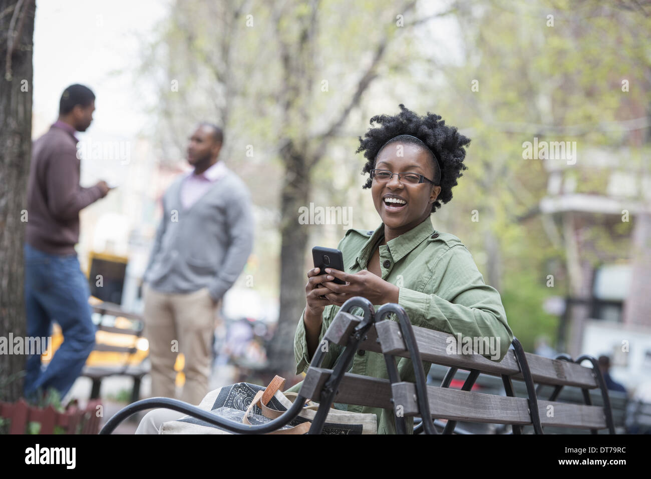 Una donna su un banco di controllo il suo telefono. Due uomini in background. Foto Stock