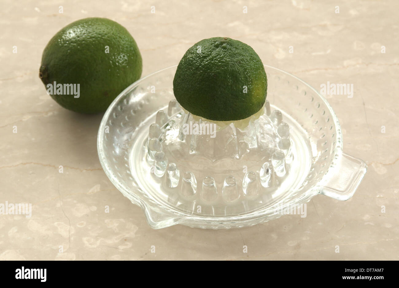 Raccogliere il succo di lime su un vetro o spremitore spremiagrumi, su una crema Sfondo marmo (3 0f una serie di 5) Foto Stock