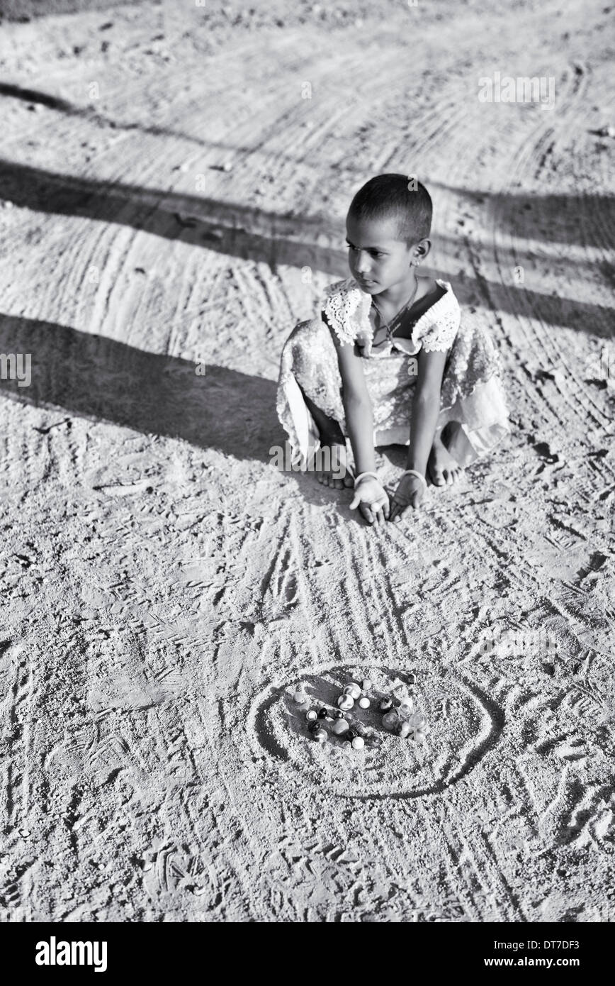 Giovane ragazza indiana la riproduzione di marmi in un territorio rurale villaggio indiano. Andhra Pradesh, India. Messa a fuoco selettiva. Monocromatico Foto Stock