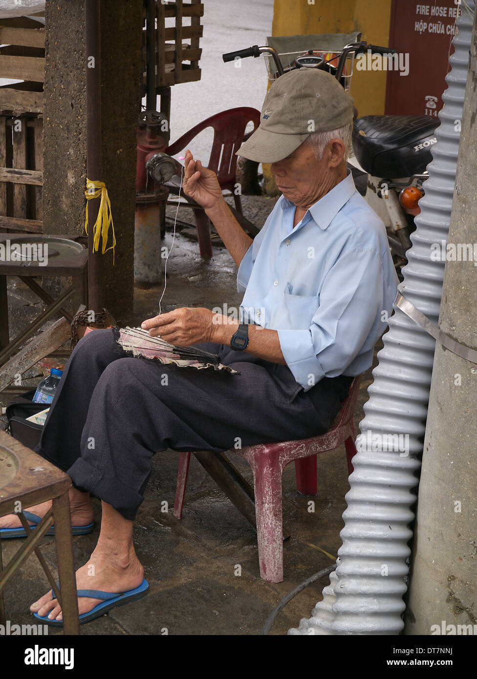 Anziani uomo seduto in street rammendo fan Hanoi Vietnam Foto Stock