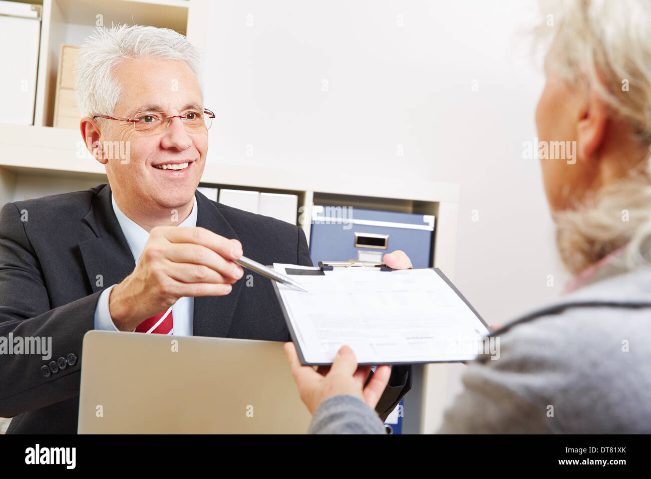 Business man dando senior donna contratto da firmare su un clipboard Foto Stock