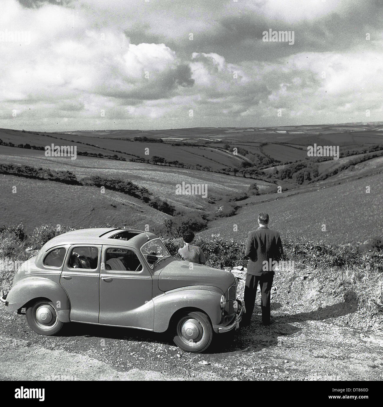 Foto storiche da anni cinquanta che mostra un uomo in piedi accanto alla sua auto parcheggiata ammirando la vista della campagna e i campi. Foto Stock