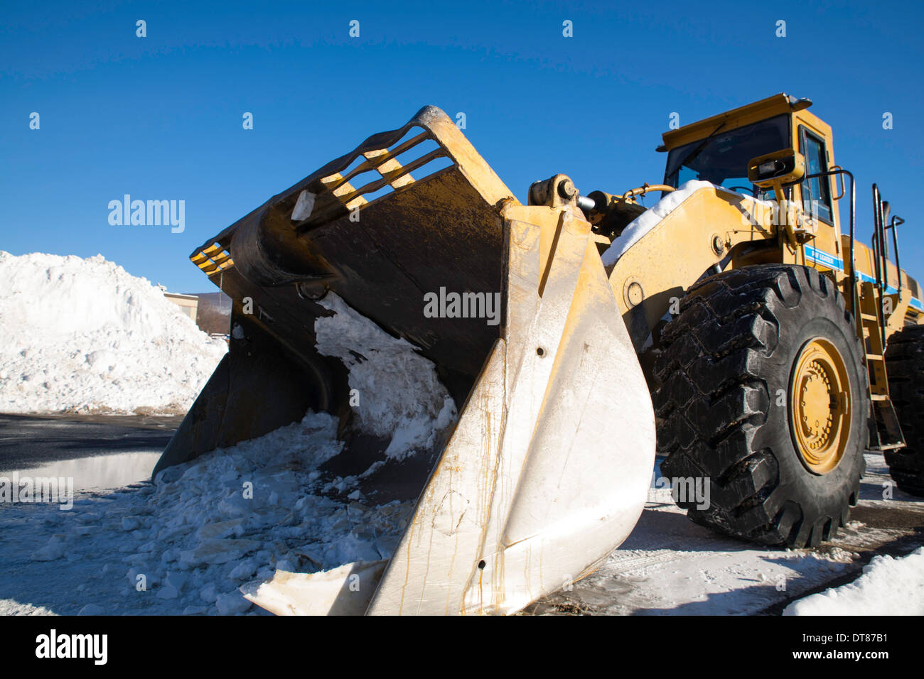 Una enorme macchina movimento terra attende in Nuova Inghilterra shopping mall parking lot impilati con le recenti neve. Foto Stock