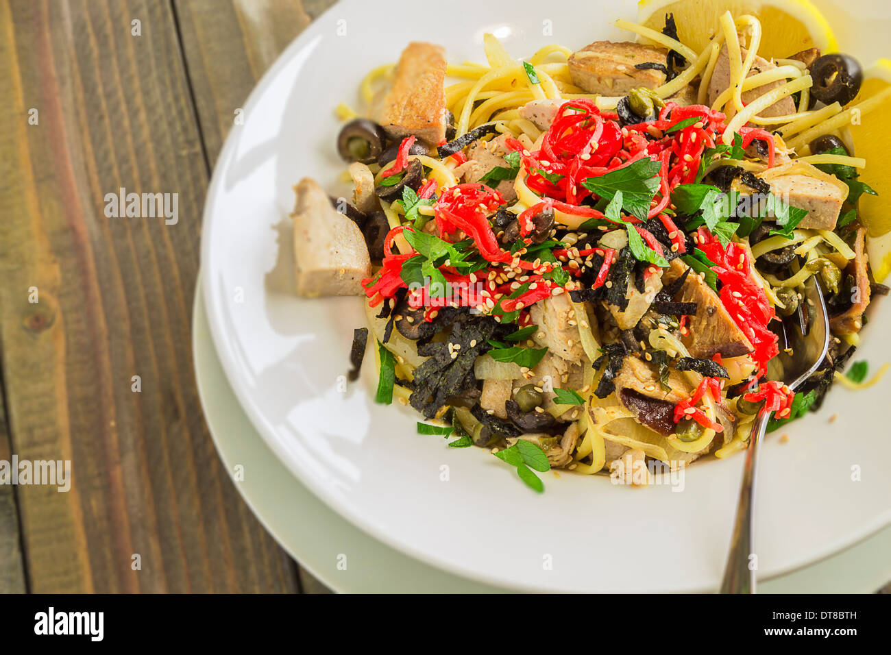 Linguine con tonno ahi e rabboccato con zenzero sott'aceto, olive nere, i semi di sesamo, prezzemolo, nori e basilico, servito con spicchi di limone Foto Stock