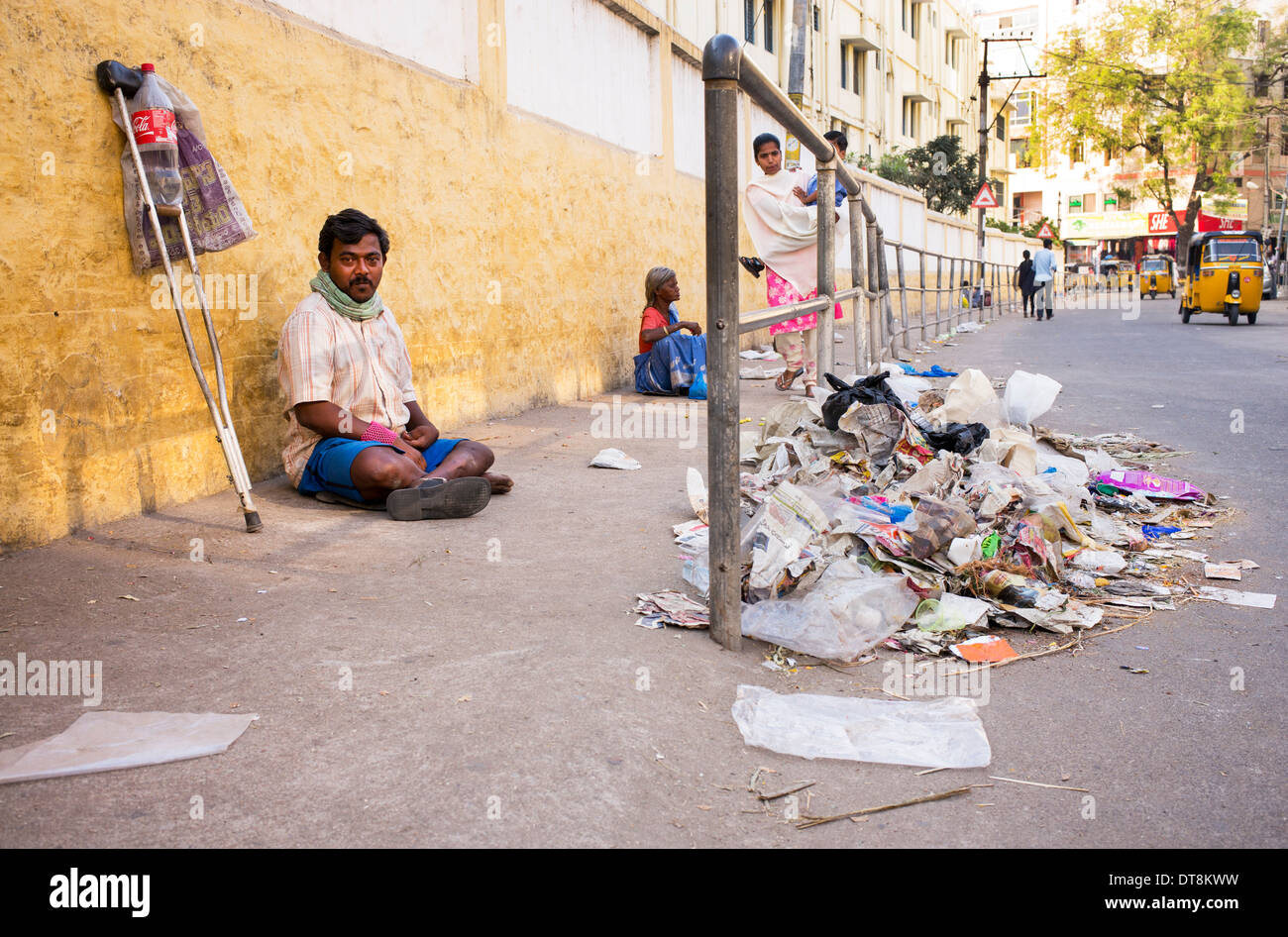 Povero uomo disabile a mendicare per un Indiano Street di fronte della spazzatura. Andhra Pradesh, India Foto Stock