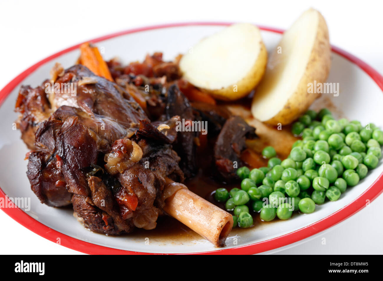 I gambi di agnello brasato con il vino, la cipolla, l'aglio, le carote, i funghi e le erbe e servito con camicia Bollite le patate e i piselli. Foto Stock