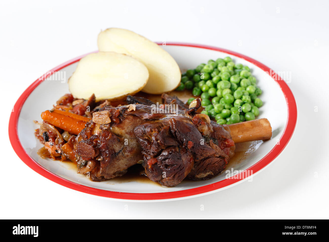 I gambi di agnello brasato con il vino, la cipolla, l'aglio, le carote, i funghi e le erbe e servito con camicia Bollite le patate e i piselli. Foto Stock
