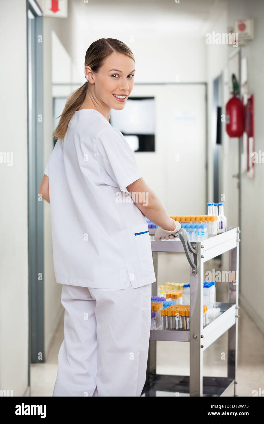 Tecnico di laboratorio spingendo un carrello medico in corridoio Foto Stock