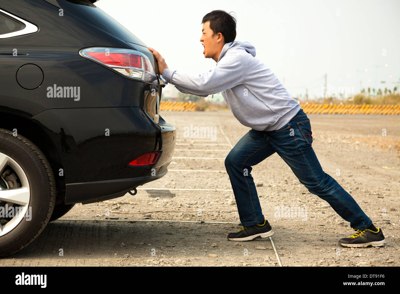 Uomo asiatico spingendo un broken auto giù per la strada della roccia Foto Stock