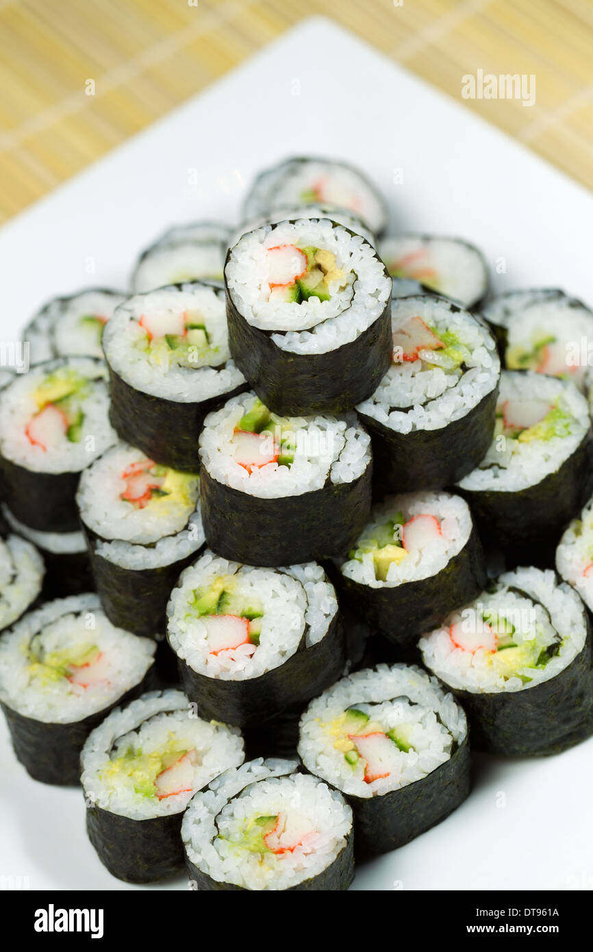 Foto verticale della piramide di sushi consistente in California i rulli a mano con naturale non colorate tappetino di bambù e piastra bianca Foto Stock