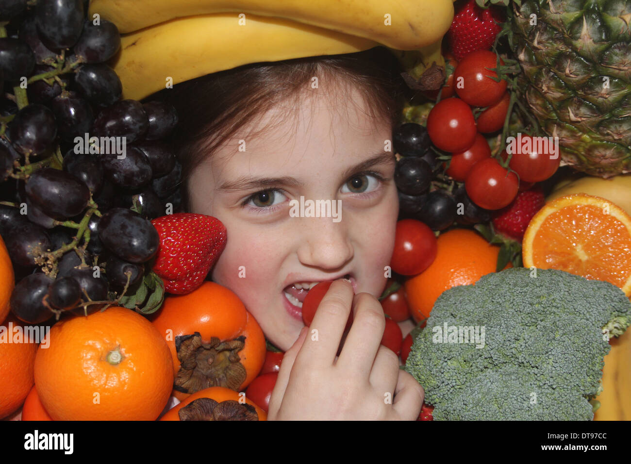 Giovane ragazza caucasica il volto circondato da frutta e verdure mangiare una mela, cinque al giorno, England, Regno Unito Foto Stock