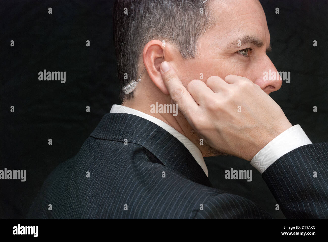 Close-up di un agente dei servizi segreti ascoltando il suo auricolare, lato. Foto Stock
