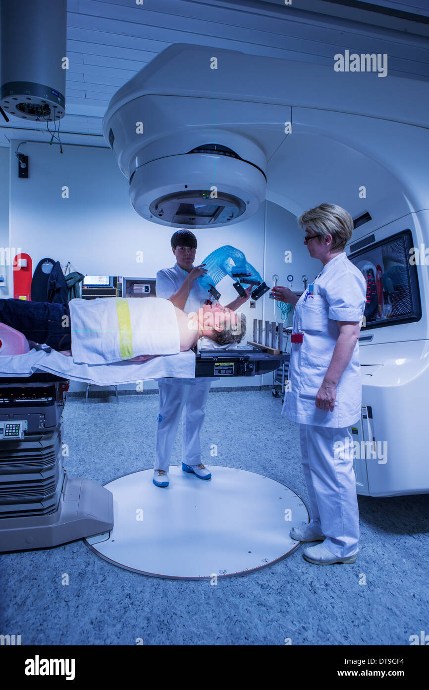 Gli infermieri mettendo una maglia maschera sul paziente di cancro appena prima del trattamento con radiazioni. Paziente di sesso maschile è sotto un acceleratore lineare. Foto Stock