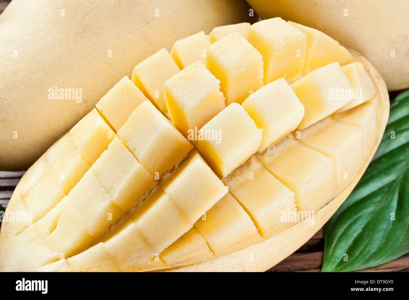 Frutti di mango, su di un tavolo di legno con fogliame verde sullo sfondo. Foto Stock