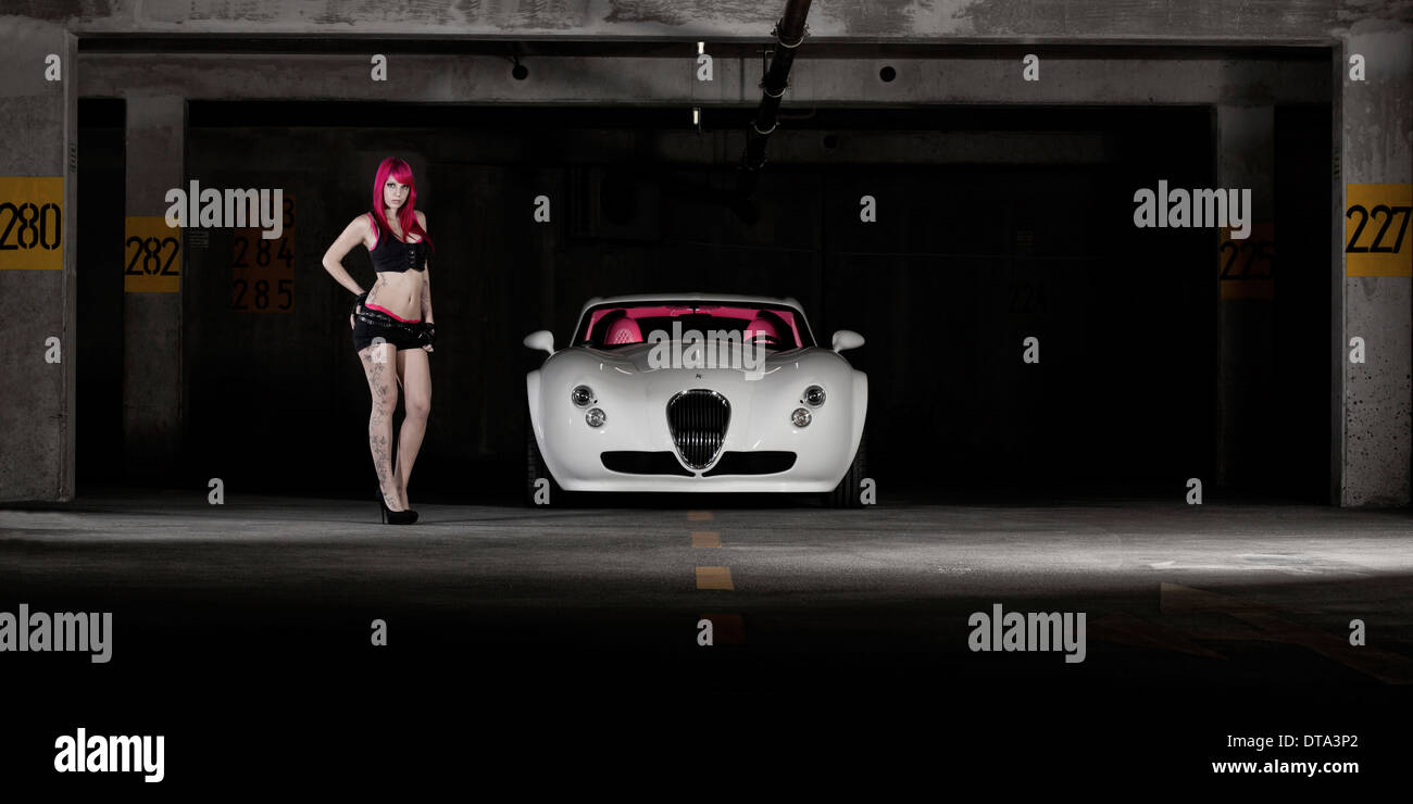 Donna con capelli rosa e tatuaggi in piedi accanto a un bianco auto sportiva Foto Stock