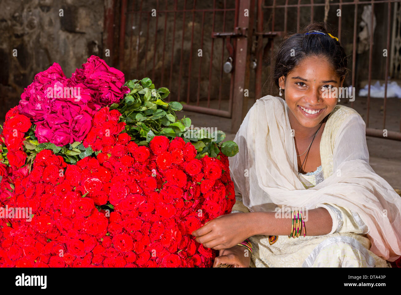 Un sorridente giovane donna in un sari bianco è la vendita di rose rosse al mercato settimanale, Nasik, Maharashtra, India Foto Stock