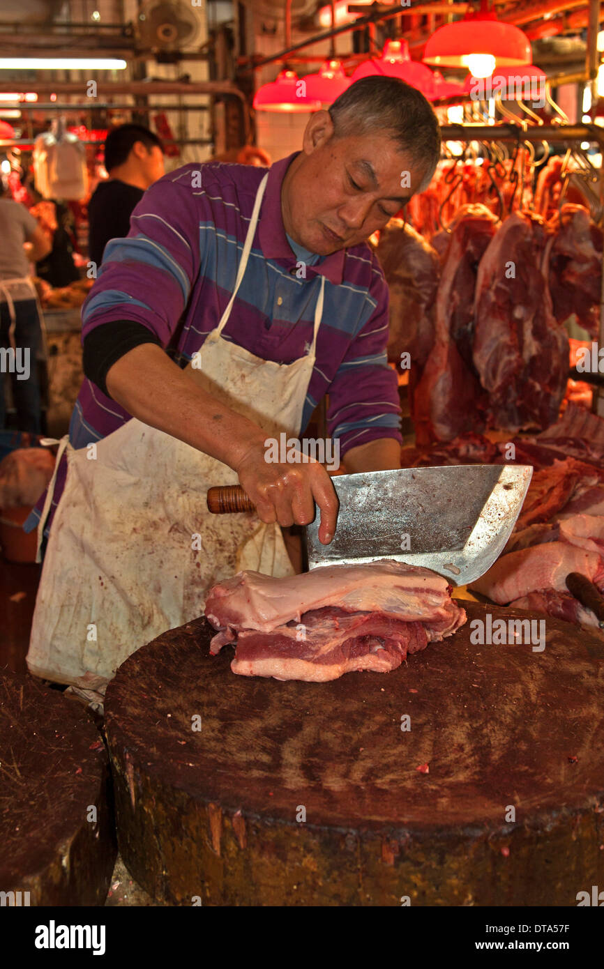 Butcher taglio pancetta di maiale con un grande coltello cinese, rosso mercato, Macau, Cina Foto Stock