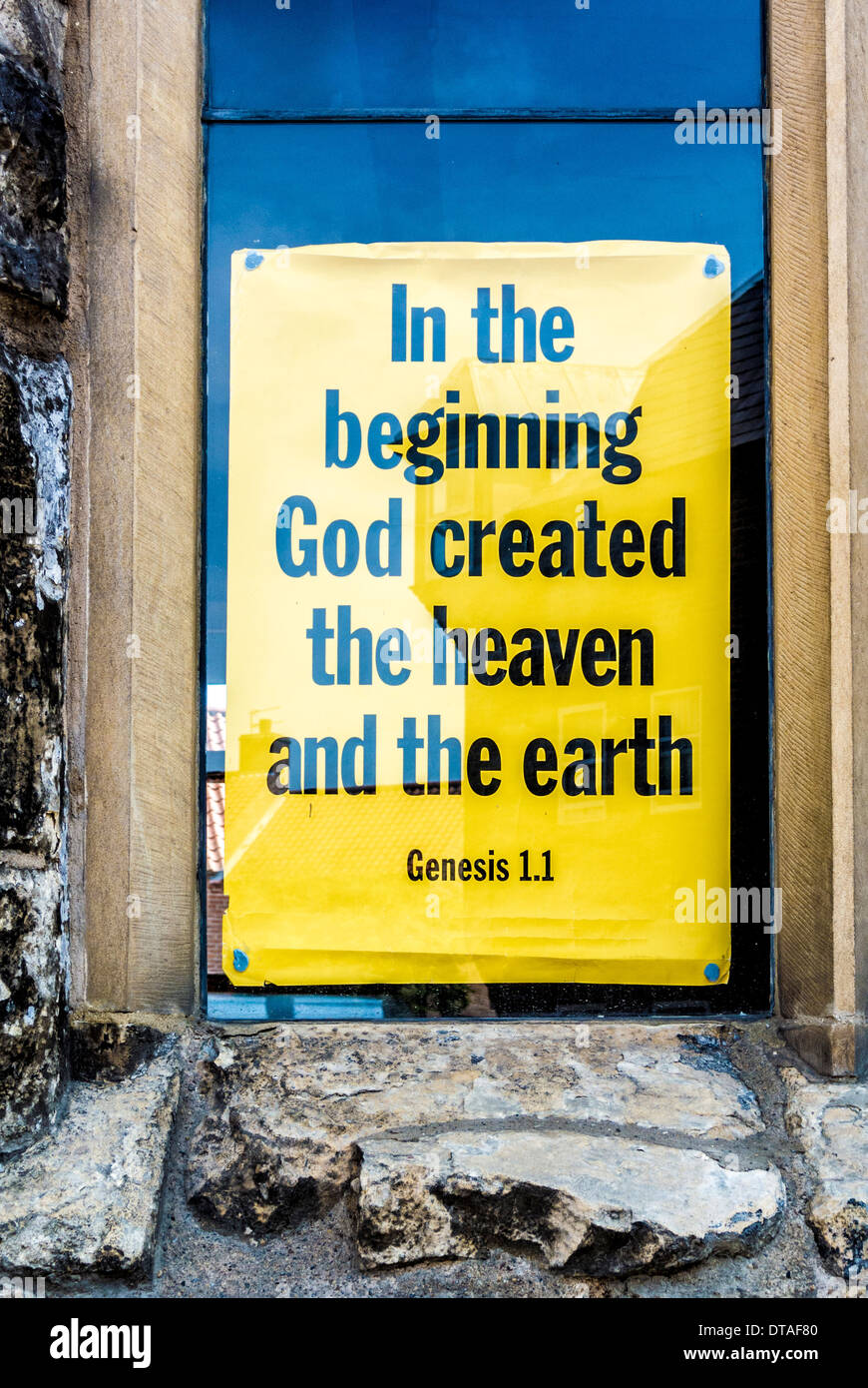 Segno giallo blu appeso in una finestra della chiesa - in principio Dio creò il cielo e la terra. Foto Stock