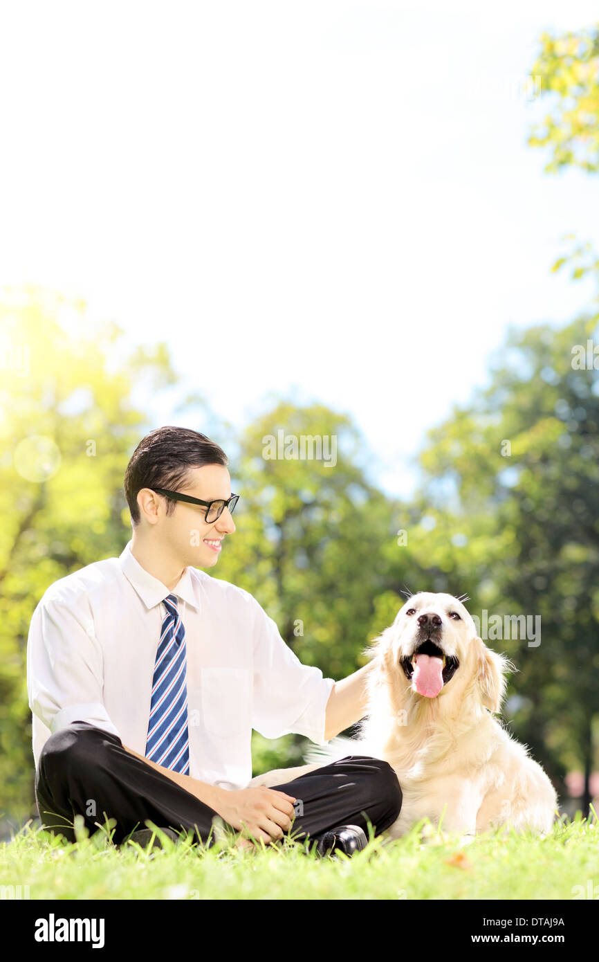 Sorridente giovane imprenditore con il suo cane seduto sul prato in un parco Foto Stock