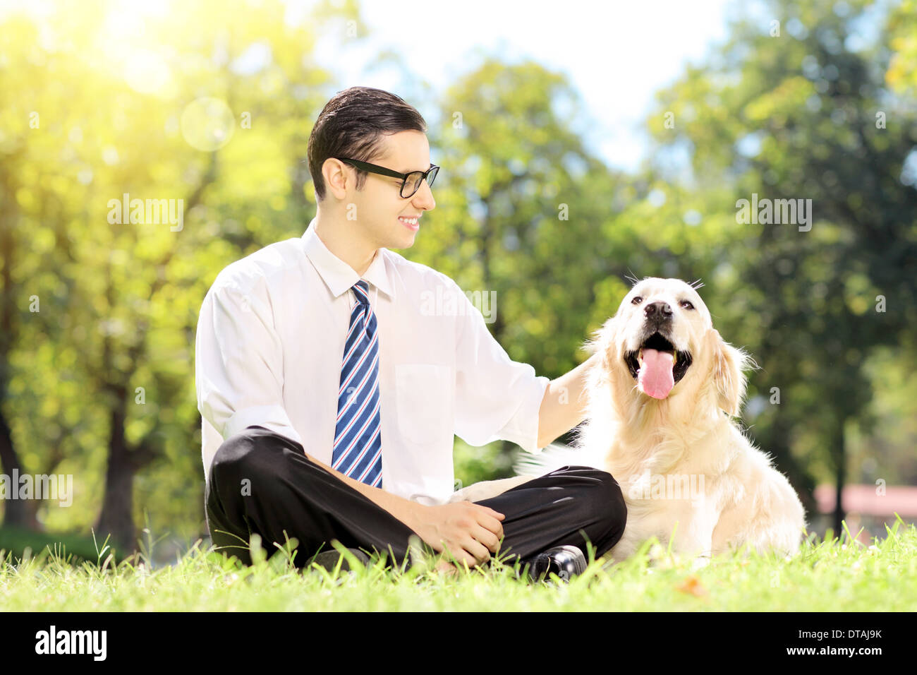 Sorridente giovane imprenditore con il suo cane seduto sul prato in un parco Foto Stock