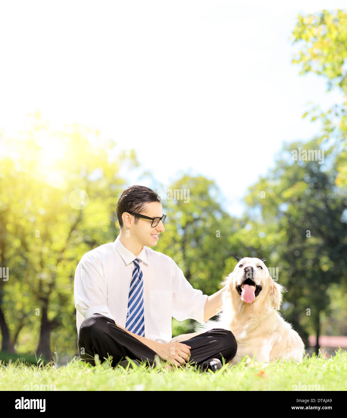 Sorridente giovane imprenditore con il suo cane seduto sul prato in un parco Foto Stock
