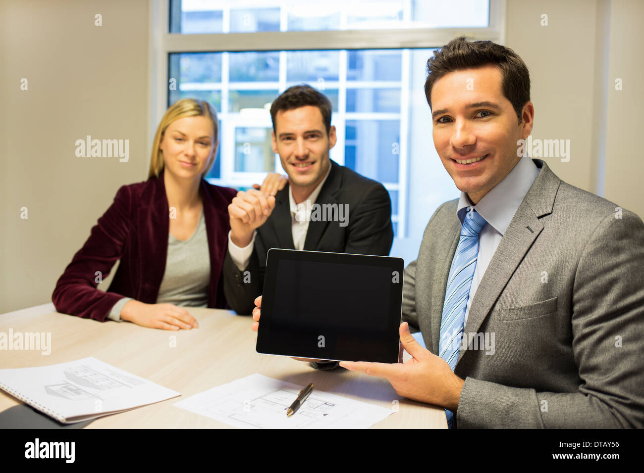 Imprenditore sorridente che mostra un nuovo progetto su tablet a coppia giovane, nuovi proprietari Foto Stock