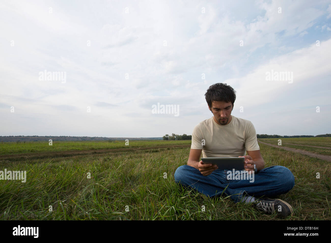 Giovane uomo seduto su erba e con tavoletta digitale Foto Stock