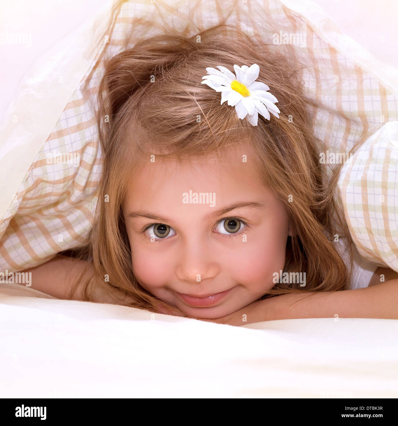 Closeup ritratto di incantevole piccola ragazza con fiore nei capelli sdraiato sul letto, ricoperta con morbido manto, nap in asilo nido Foto Stock