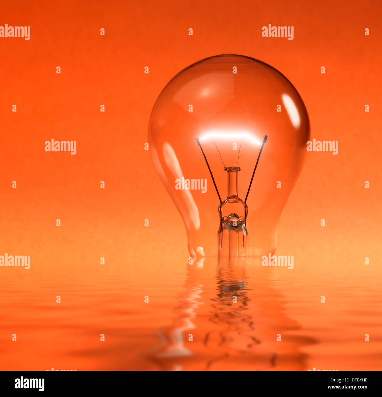 Un parzialmente sunken incandescente lampadina elettrica riflettente sulla superficie di acqua in arancione indietro Foto Stock