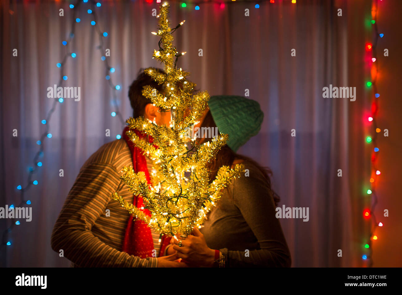 Coppia giovane kissing dietro illuminato albero di natale Foto Stock