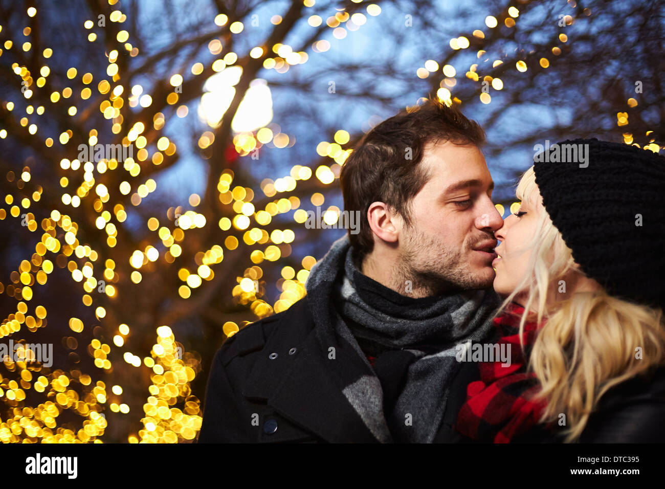 Coppia giovane baciando di fronte all'aperto le luci di Natale Foto Stock