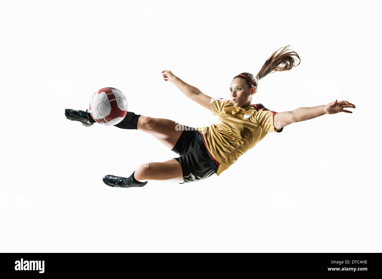 Studio shot di femmina giovane giocatore di calcio calci palla metà aria Foto Stock