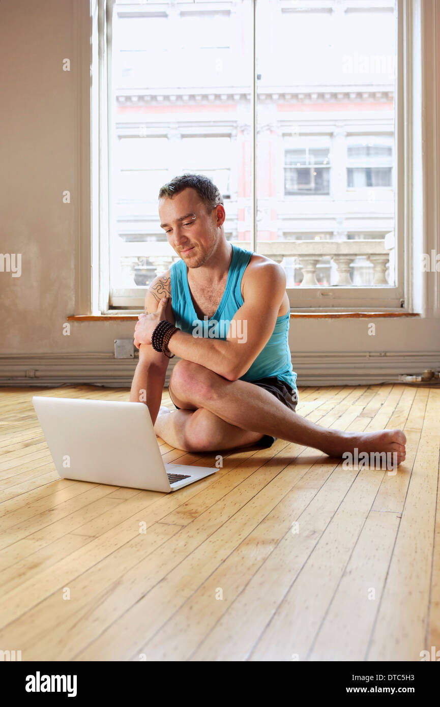 Metà uomo adulto utilizzando portatile mentre in Cowface Yoga posa Foto Stock