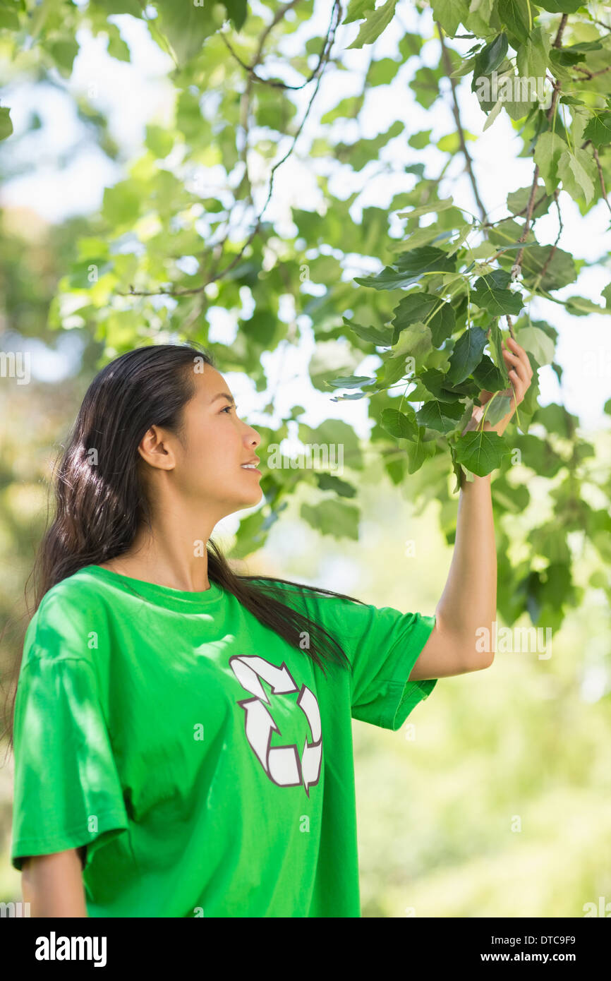 La donna nel riciclaggio verde t-shirt toccando le foglie in posizione di parcheggio Foto Stock