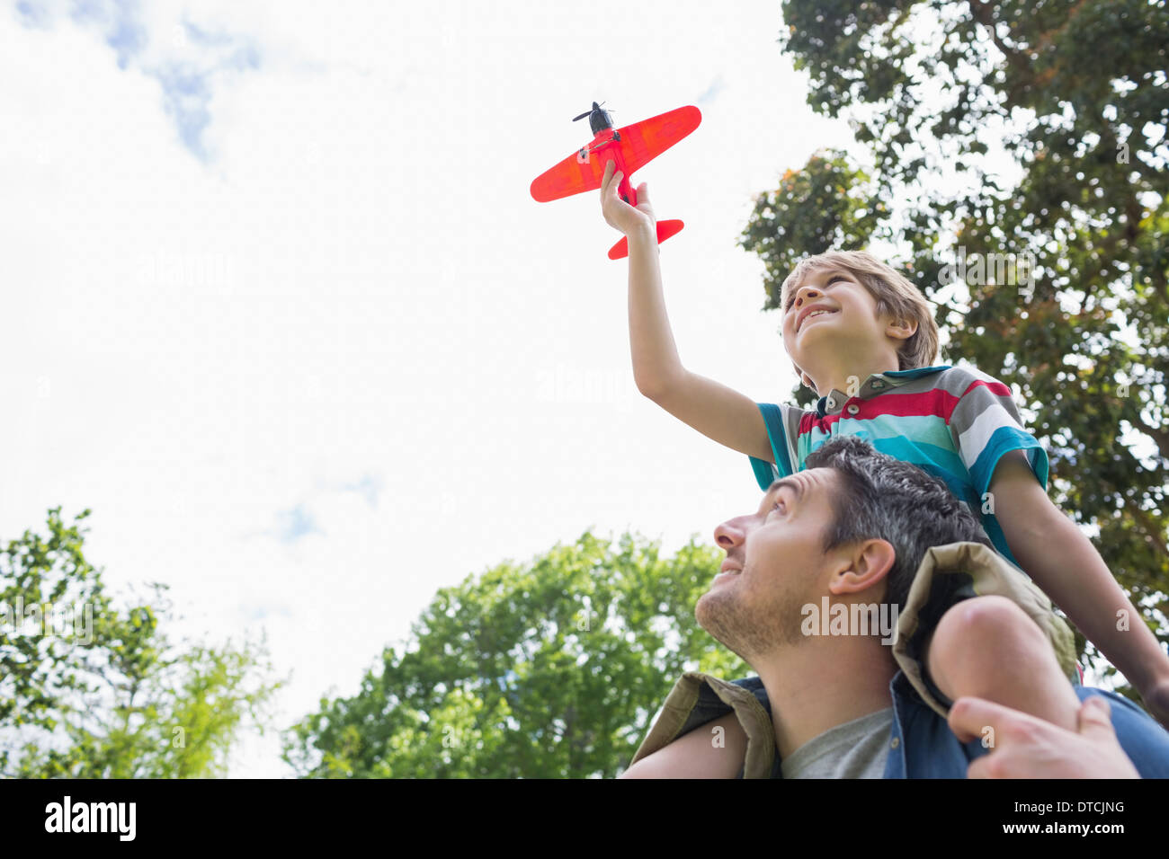 Ragazzo con aeroplano giocattolo seduto sul padre di spalle Foto Stock