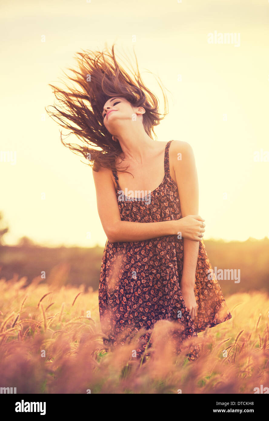 Bella giovane donna all'esterno. Modello romantica in abito di Sun nel campo oro al tramonto. Gorgeous capelli lunghi che soffia nella Sunligh Foto Stock