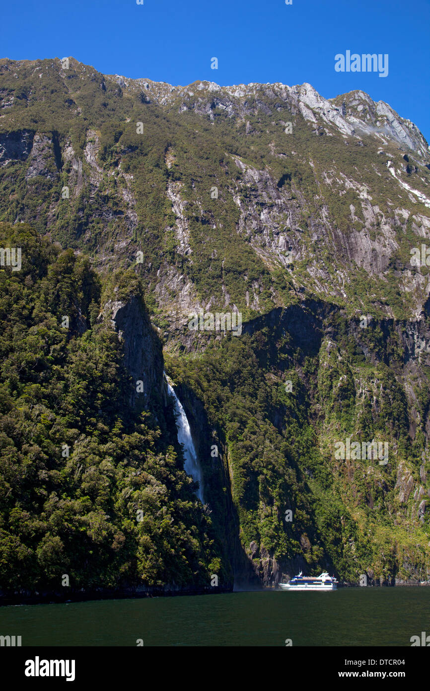 Imbarcazione turistica accanto a cascata sul Milford Sound, Fiordland, Isola del Sud, Nuova Zelanda Foto Stock