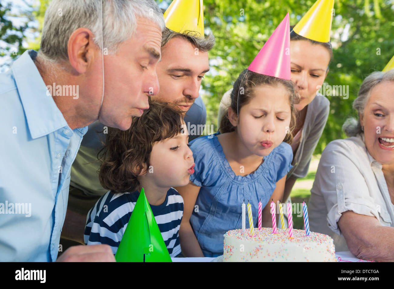 Famiglia estesa nella parte cappelli soffiando torta di compleanno Foto Stock